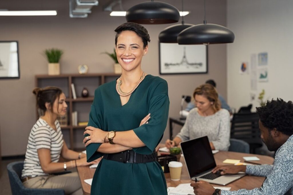 Work in Dubai confident woman standing in office while team works in background