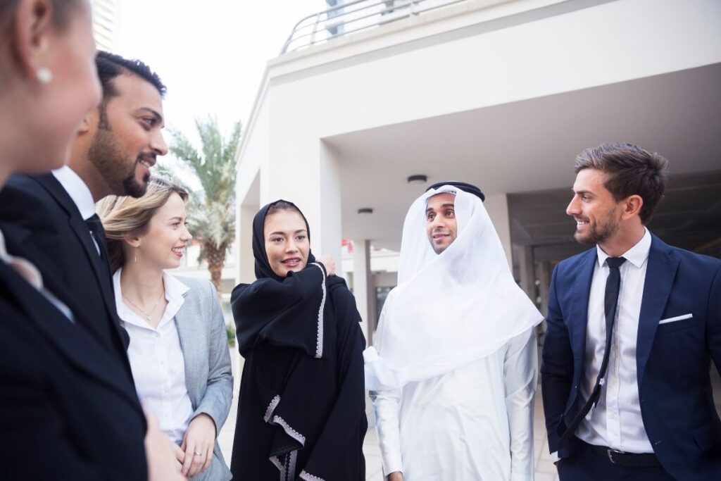 Internationale Geschäftsleute und Emirati im Gespräch vor modernem Gebäude in Dubai zum Thema Arbeitsvisum Dubai