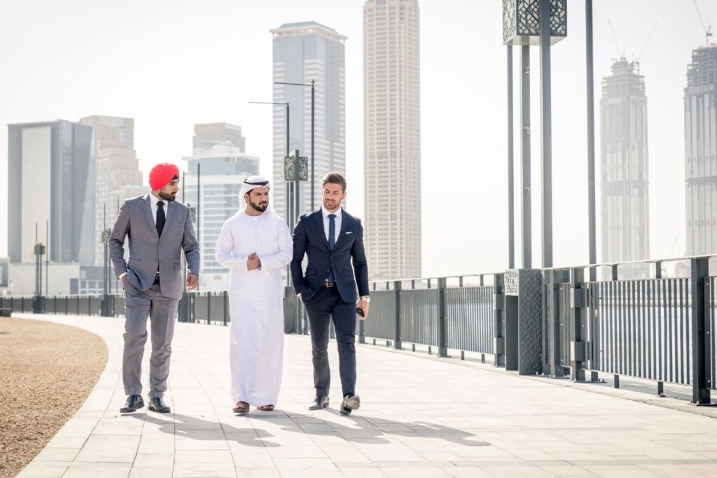 Drei Geschäftsleute gehen vor der Dubai Skyline gemeinsam über eine Promenade und besprechen das Dubai Investorenvisum.