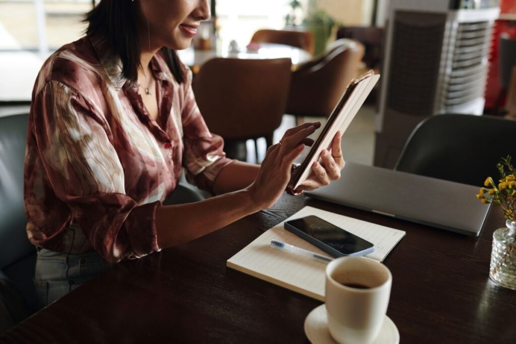Woman working on tablet and laptop in a café representing remote work and flexible lifestyle Dubai Golden Visa