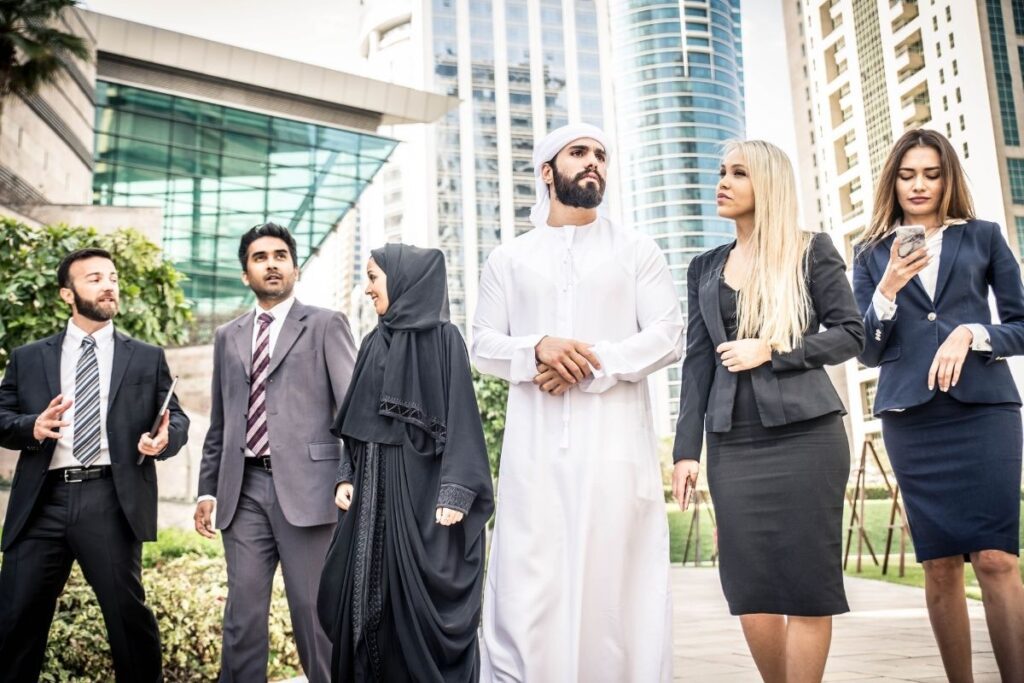 Geschäftsleute in Dubai in Business- und traditioneller Kleidung vor moderner Architektur beim Austausch über Karriere und Aufenthalt Golden Visa Dubai