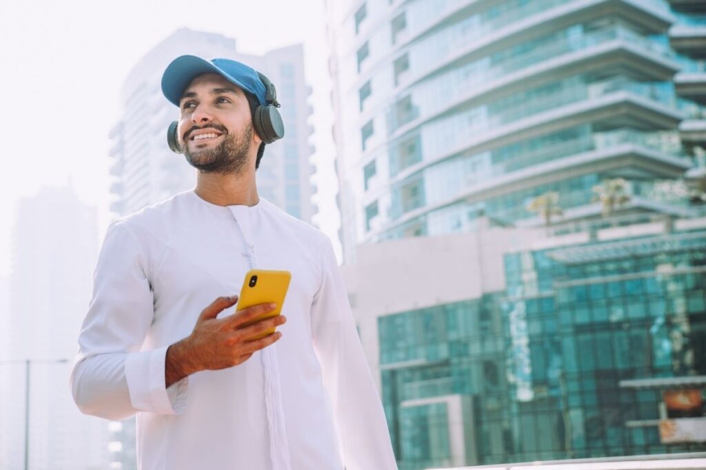 Mann in traditioneller Kleidung nutzt Smartphone vor moderner Skyline und profitiert vom Green Visa Dubai.